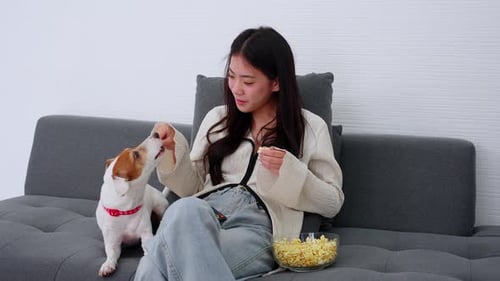 Woman Feeds Dog Popcorn on Gray Sofa
