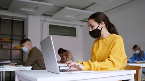 Young multi ethnic students in university classroom wearing face masks looking at camera