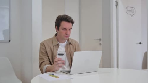 Young Adult Works at Desk with Laptop and Phone