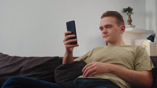 Young Adult Relaxing on Couch with Smartphone
