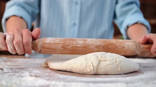 Baker Rolling Raw Dough on Table in Home Kitchen or Professional Bakery Closeup View of Hands