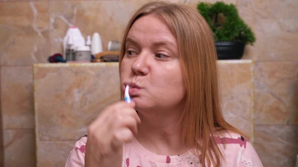 Infantile woman in pink pajamas brushing her teeth humming naively ...
