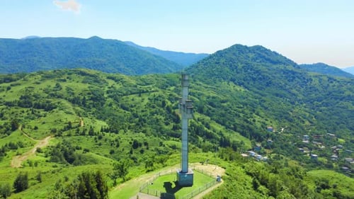 Close-up view from drone of Orthodox cross on mountain against sea against sun,