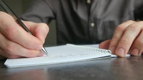Männliche Hände, die mit einem Kugelschreiber Notizen in ein Notizbuch schreiben