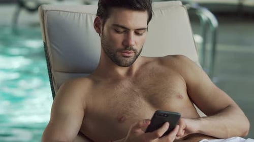 Handsome businessman relaxes by pool at luxury spa hotel using mobile phone