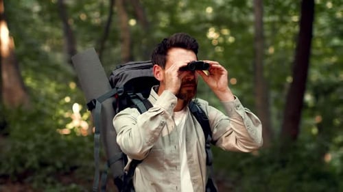 Man With Light Skin Uses Binoculars While Hiking in a Forested Area