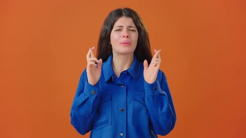 Woman Gesturing Hope and Praying Against Orange Backdrop
