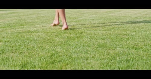 Mujer joven con los pies descalzos caminando sobre césped verde