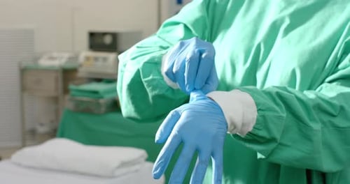 Midsection of caucasian female surgeon wearing medical gloves in operating theatre, slow motion