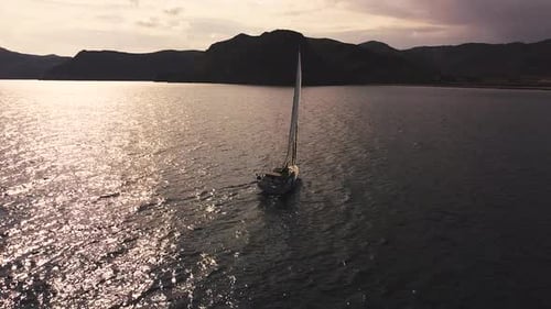 Sailboat sailing by coastline seashore against sunset and mountains. Sail boat in the south coast