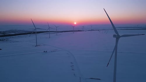 Aerial View of a Wind Farm in a Snowy Landscape at Sunset Large Wind Turbines Stand Tall Against the