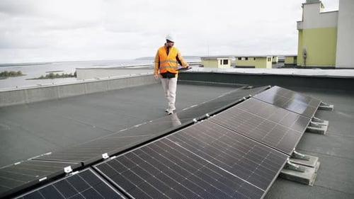 Man Inspecting Solar Panels on Rooftop with Tablet
