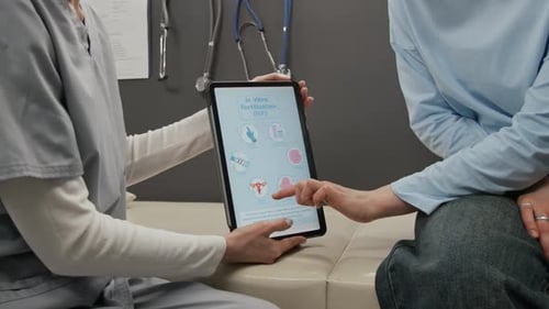 Femme décrivant le processus de FIV pointant vers une tablette numérique tenue par une femme médecin