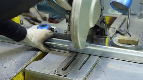 Industrial Worker Using a Metal Saw to Cut Steel Profiles in a Factory Setting