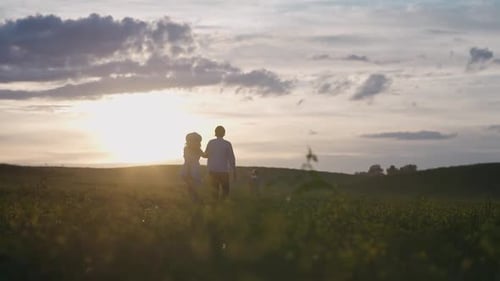 Handheld Family Outdoor Recreation Couple are Walking Through a Field of Rapeseed Holding Hands Boy