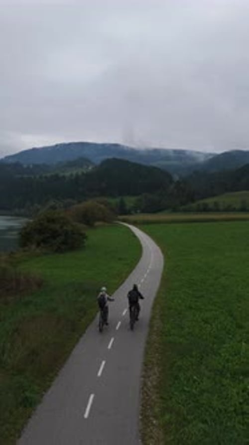 Couple Biking, Riding E-Bikes On Bike Path In Countryside Along River, Aerial Vertical View