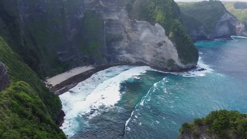 Waves crashing on a small beach surrounded by cliffs in Bali. Tropical island drone footage.