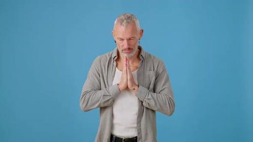 Emotionaler Mann faltet im Studio die Hände in die Gebetsposition