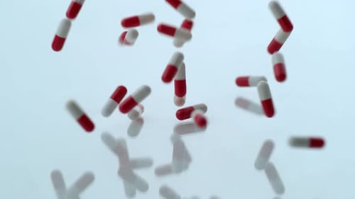 Red and White Pills Falling Against White Background
