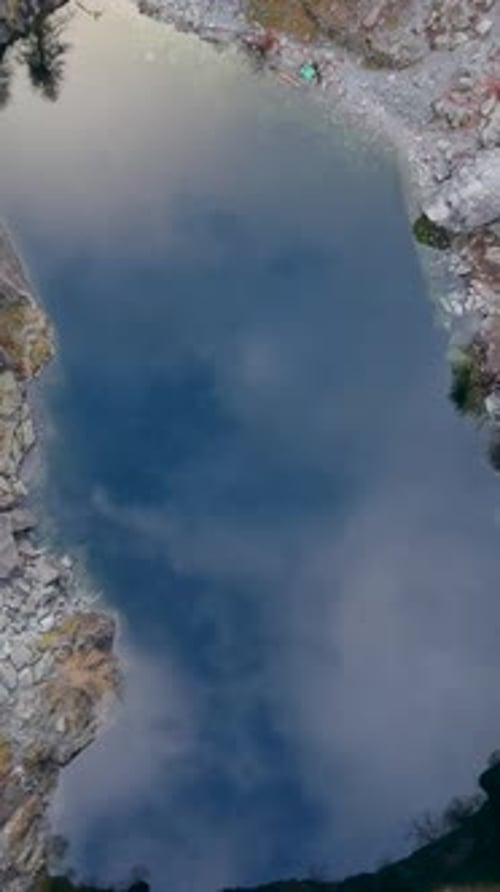 Vertical Top-Down Descent Over Quarry Lake with Mirror-Like Cloud Reflections and Steep Slate Walls
