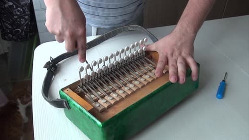 Man Repairs Wood Accordion with Screwdriver