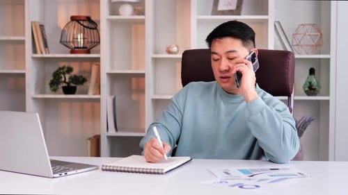 Smart Asian Entrepreneur Talking on Smartphone Working on Laptop in Office