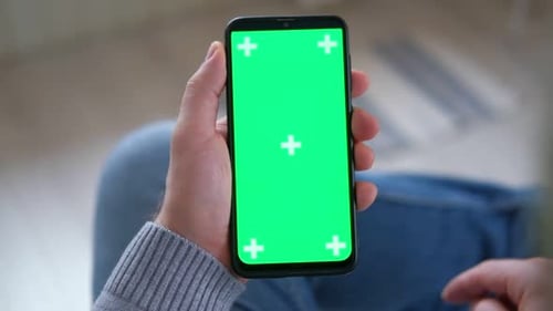 Young Man Sitting at Home Holding Smartphone Green Mockup Screen in Hand Male Person Using Chroma