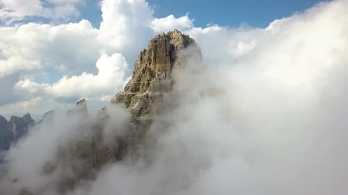 Aerial zoom in closeup of a Single Mountain Peak coming through the fluffy clouds on a sunny day, Dr