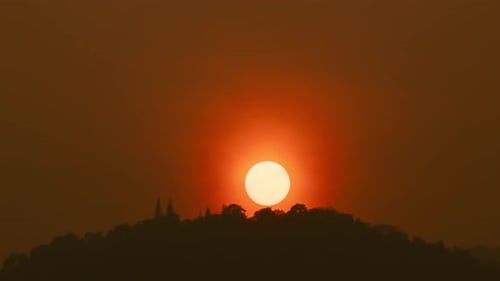 Time lapse of the sun setting over hills that are covered with clouds, in the style of smokey backgr