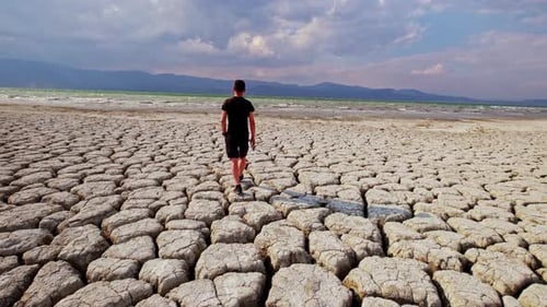 Young Adult Walks on Cracked Earth By Lake