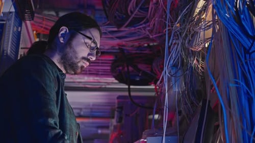 Man Works Amongst Tangled Wires in Server Room