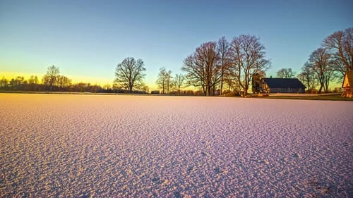 Sunset over a winter landscape with a large snow-covered meadow.