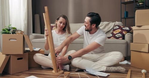 Serious Concentrated Woman and Man Trying to Decorate Furnish New Wooden Floor Lamp Moving in