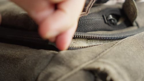 A hand zipping up a brown canvas bag in a close-up shot