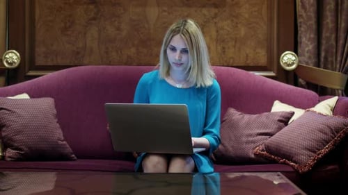 Beautiful Woman Sitting on Luxury Sofa and Working on Notebook Computer. Young