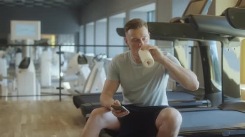 Man Using Phone on Water Break in Gym