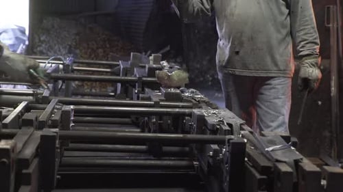 Side view of people pouring liquid metal into casts in a factory,