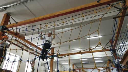 a Brave Boy Climbs an Obstacle in the Form of a Rope Web in a Rope Park Indoors