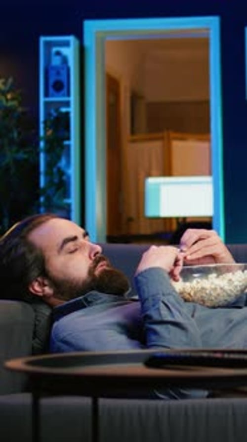 Bearded Adult Eats Popcorn Laying on Couch