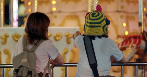 Rearview of two friends exploring carnival carousel as they talk and point after school