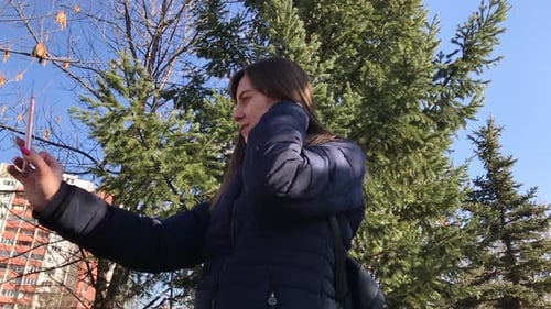 Slowmo of young girl taking selfies with a smartphone using front camera in a city park. medium left