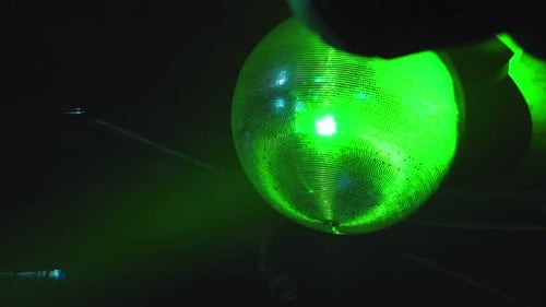 A large disco ball hanging from the ceiling, spinning with different colors of lighting reflecting i