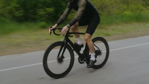 Bicyclist in Black Tracksuit Activewear Rides Bike Along Road