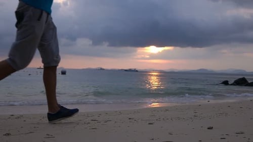 Man runs silhouetted on sandy beach at sunset in super slow motion