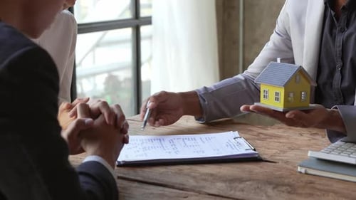 Modelo de casa com agente e cliente discutindo um contrato para comprar, obter seguro ou empréstimo