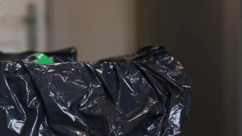 Static shot of rubbish being thrown into a nearly full bin with a black bin liner