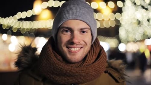 Happy young man blowing on hands freezing at christmas market in winter evening