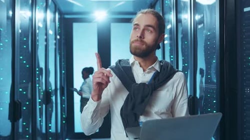 A Professional in a Data Center Works with a Laptop and a Skilled Female Technician