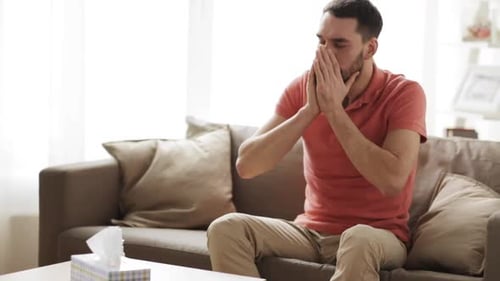 Adult Man with Beard Sneezes on Couch Indoors