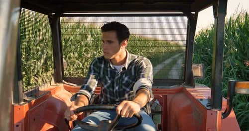 Portrait of a beautiful young farmer (student), sits inside in the tractor cabin, rides the field,